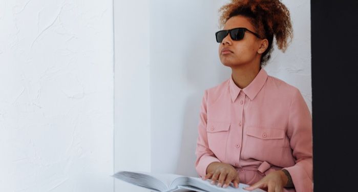 light-skinned blind Black woman wearing pink and reading braille
