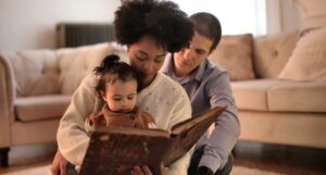a brown-skinned Black woman and fair-skinned white man reading to their light-skinned baby
