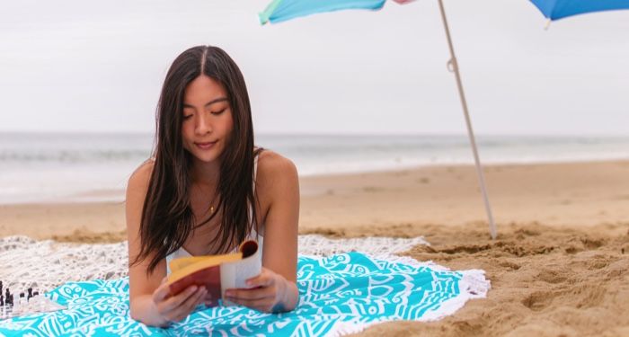 tan-skinned woman with long, dark hair reading a book on the beach