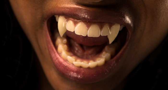 a photo of a person with dark skin and vampire teeth baring their teeth
