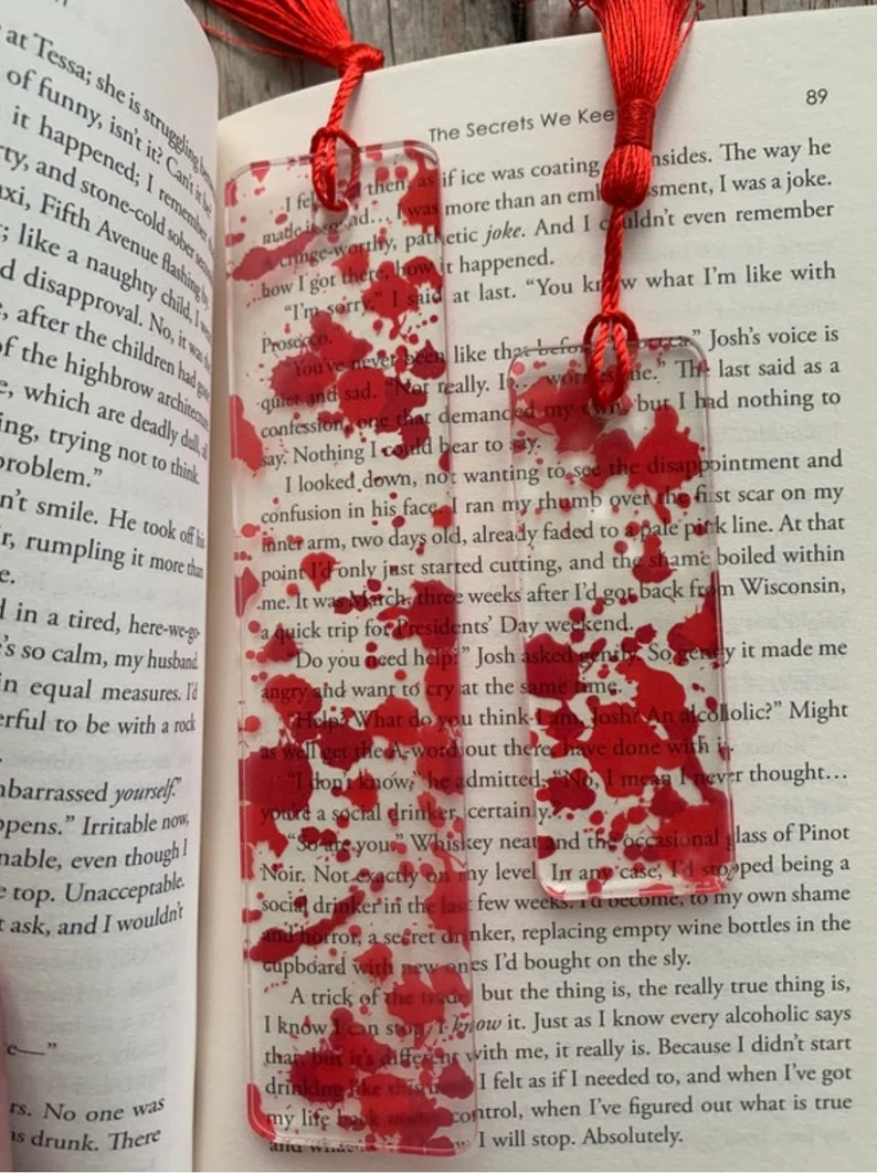 Photo of an open book with two bookmarks on it, the bookmarks resemble blood-spatters and one is smaller than the other, with a string at the top. 