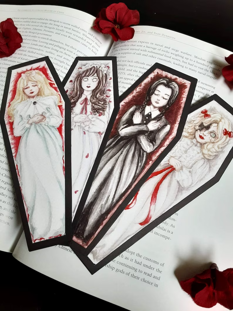 Photo of an open book with four coffin-shaped bookmarks on the pages, each a different girl. 