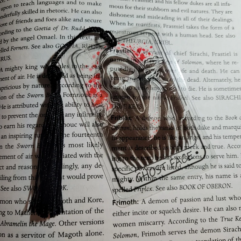 Photo of a page with text with a clear bookmark shaped like a tarot card with the image of Ghostface on it and a small string coming from the top.
