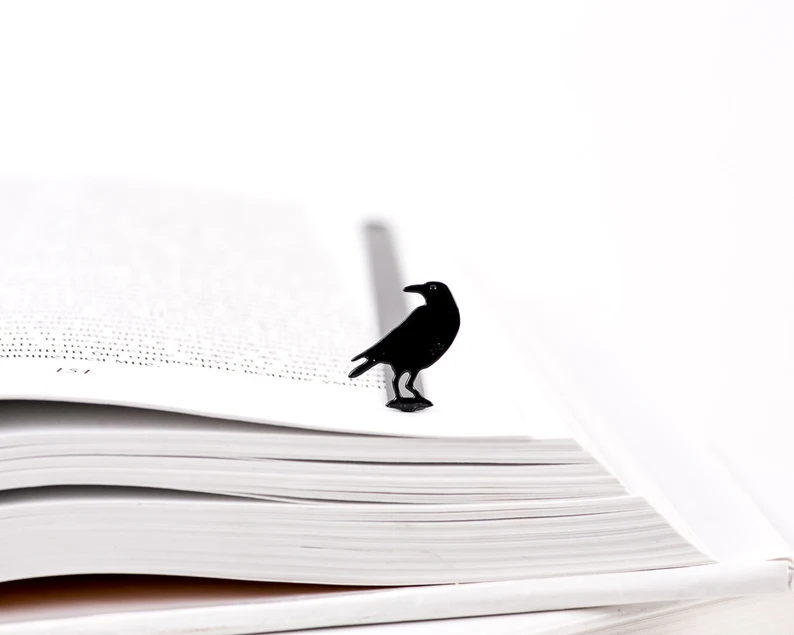 Photo of a small raven bookmark placed on an open book.