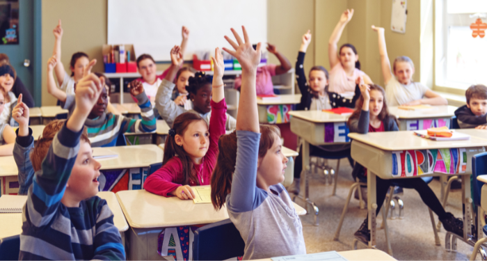 a photo of a classroom full of kids eagerly raising their hands
