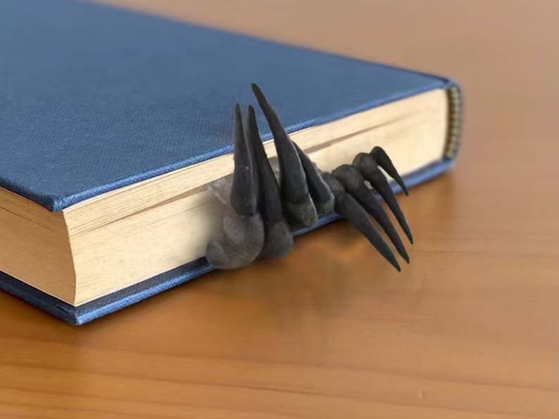 Photo of a closed book with a blue cover and coming out from the bottom, stuck between the pages are two black claws. 