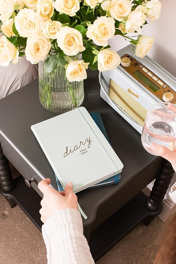 Busy B planner on nightstand with white roses
