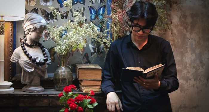 fair-skinned Asian man reading a book beside rustic and pretty decorations