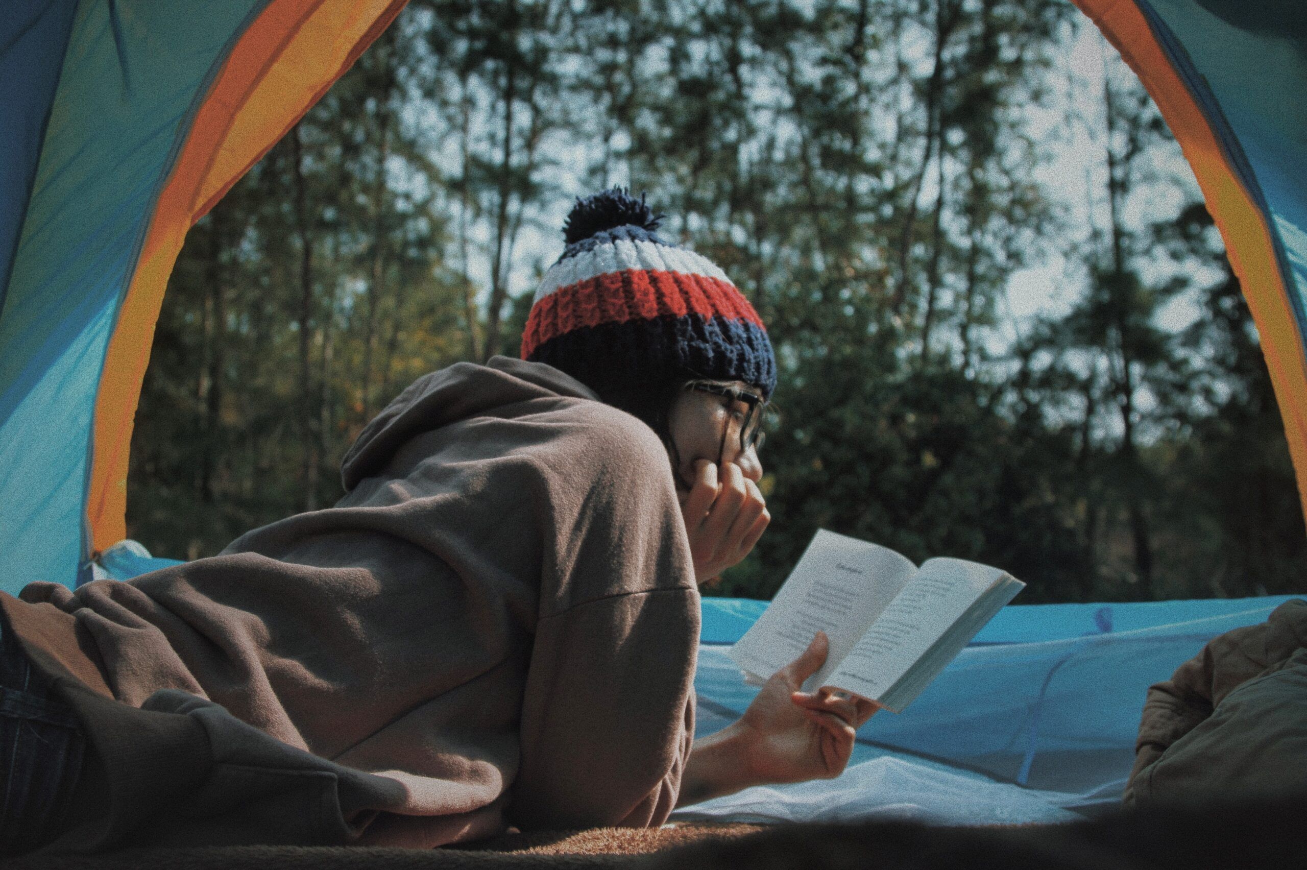 A person reading a book in a tent with forest behind them. 