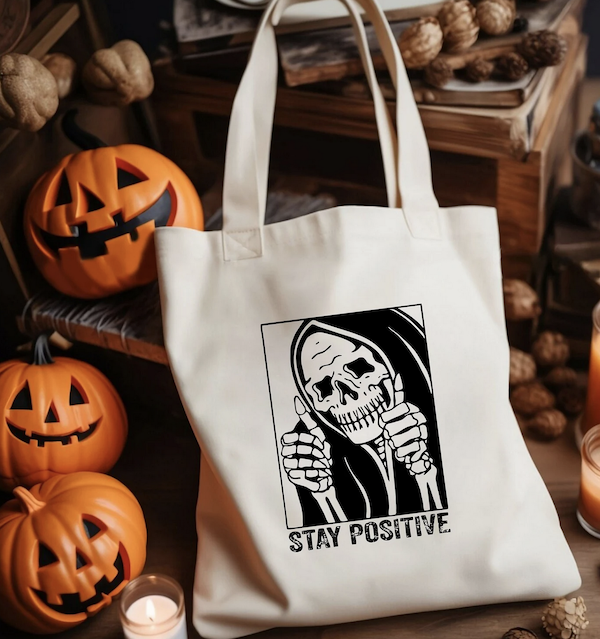 canvas tote bag screen printed with a skeleton giving the thumbs up and text saying "stay positive"