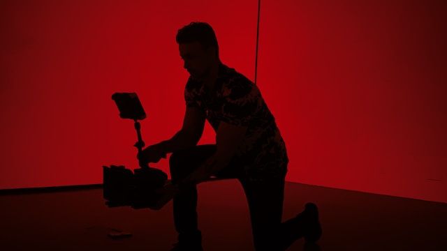 silhouette of a person holding a professional video camera against a red lit background