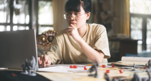 a photo of an Asian woman playing a TTRPG and consulting her laptop