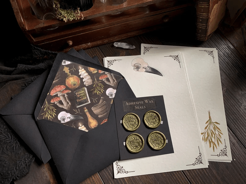 Photo of a writing set with loose sheets, envelopes and wax seals, with different designs such as bones, a snake tooth, mushrooms, pumpkins and books.
