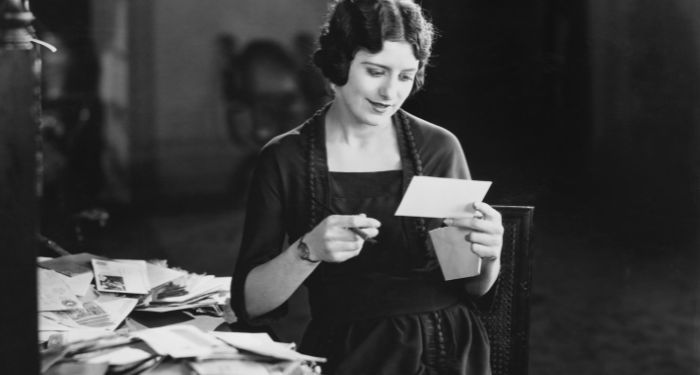 black and white image of a women reading a letter standing next to a pile of mail