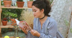 a lighter-skinned Asian woman reading by some potted plants