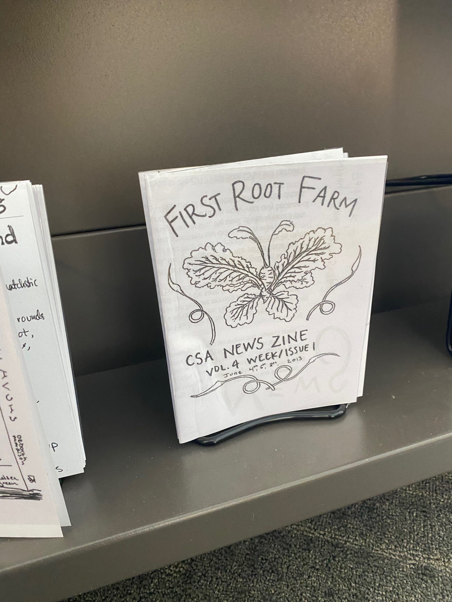 A copy of the small First Root Farm CSA New Zine displayed on the library zine shelf.