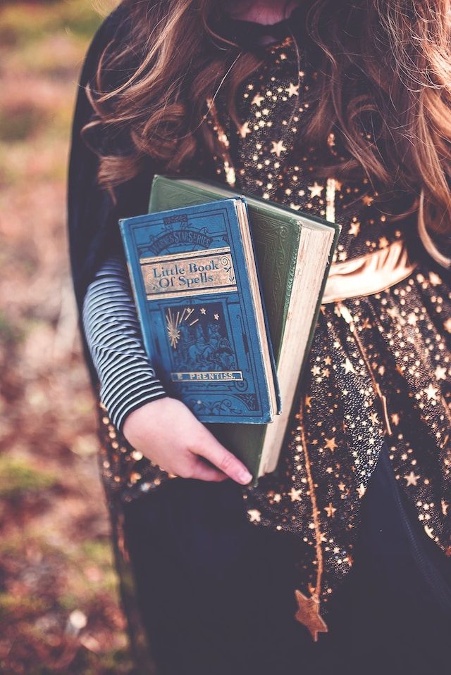 a woman wearing a cape and starry dress holding two books of spells