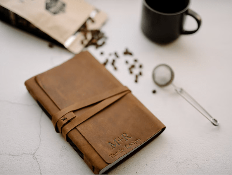 Photo of a leather notebook with a leather strap closing it and some text  engraved on the cover