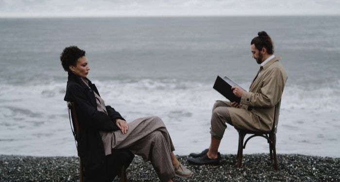two people sitting in chairs opposite each other on a chilly, rocky beach
