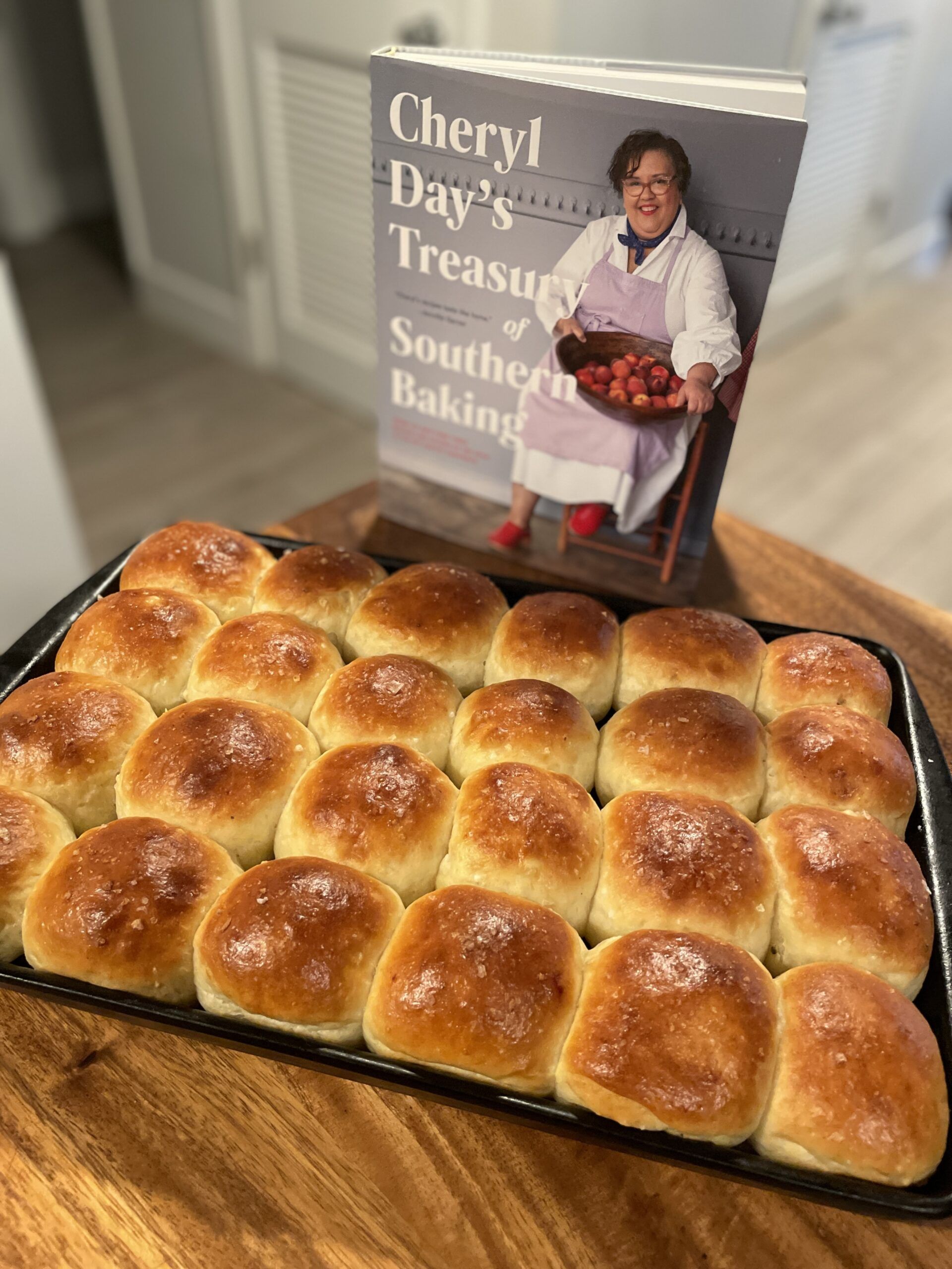 A pan of deep golden dinner rolls in front of the cookbook Cheryl Day's Treasury of Southern Baking