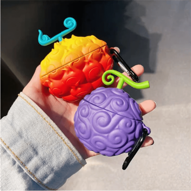 Photo of a hand holding two Airpod cases shaped like devil fruits, one purple and one red and yellow.