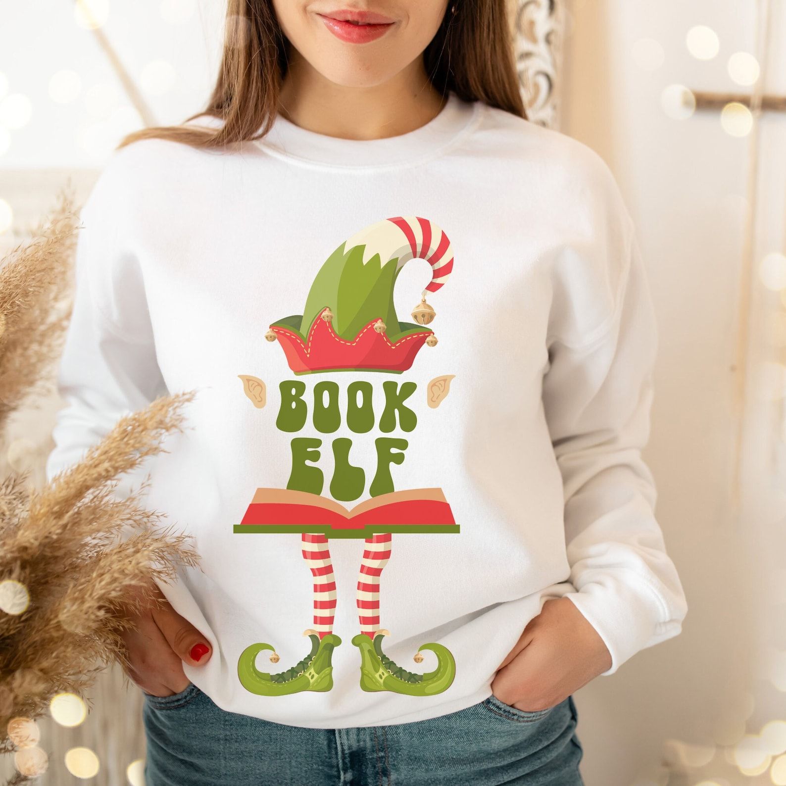 A white sweatshirt with elf legs and hat that reads "book elf"