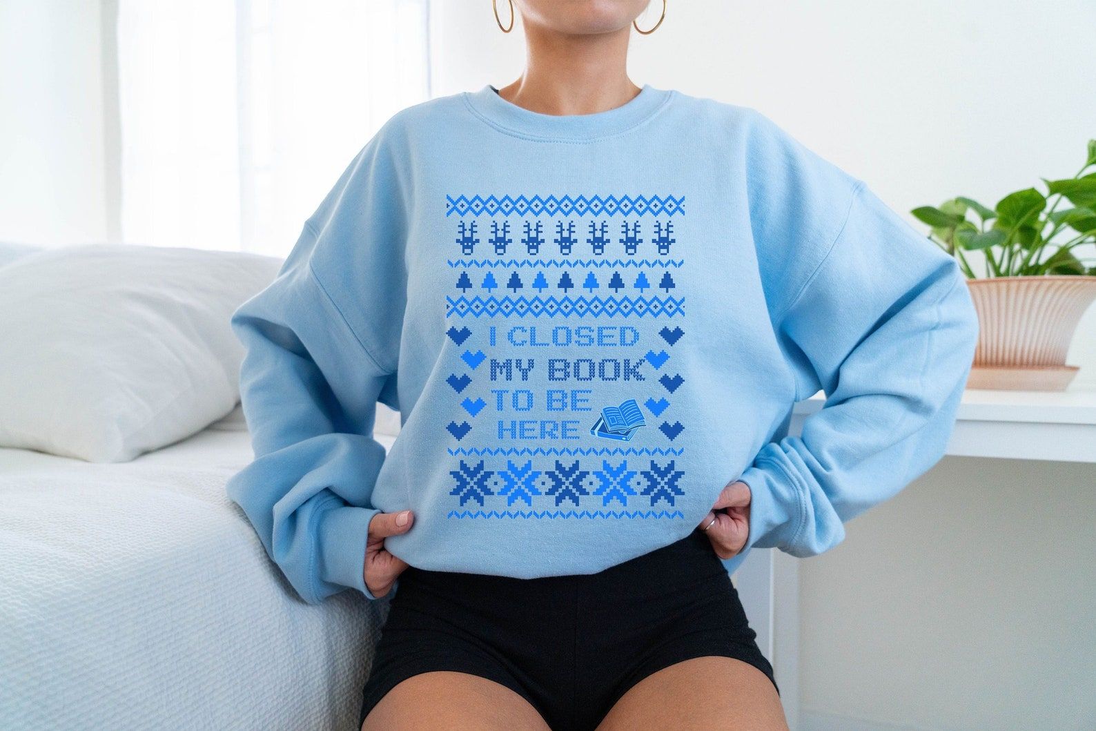 A blue sweater with a knit motif that reads "I closed my book to be here"
