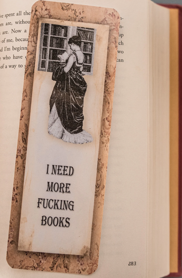 a book mark with a vintage image of a woman reading that says "I need more fucking books"
