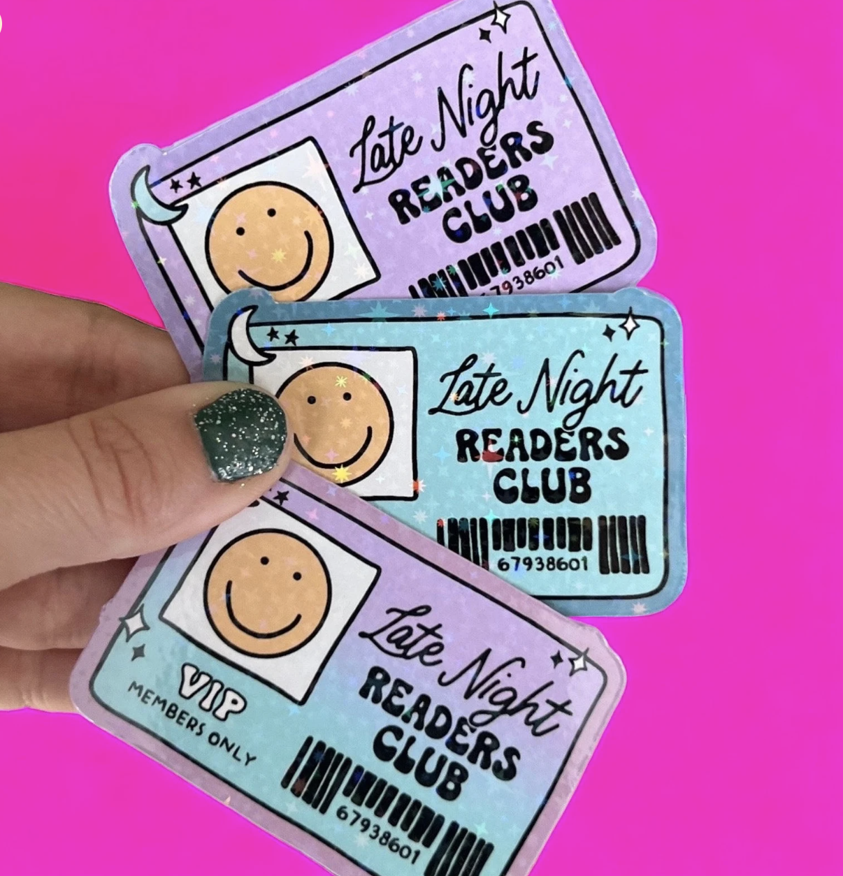 A hand holding three stickers that read 'Late Night Reading Club.'