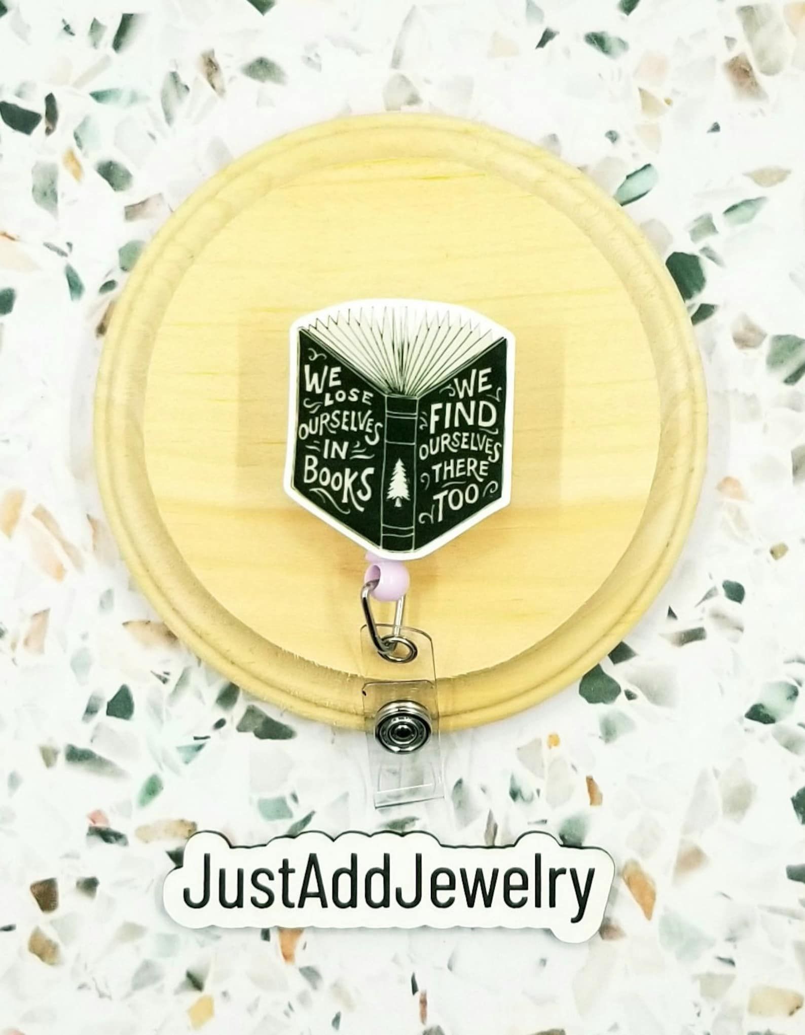 A badge reel that is an open book with the words "We lose ourselves in books, we find ourselves there too."