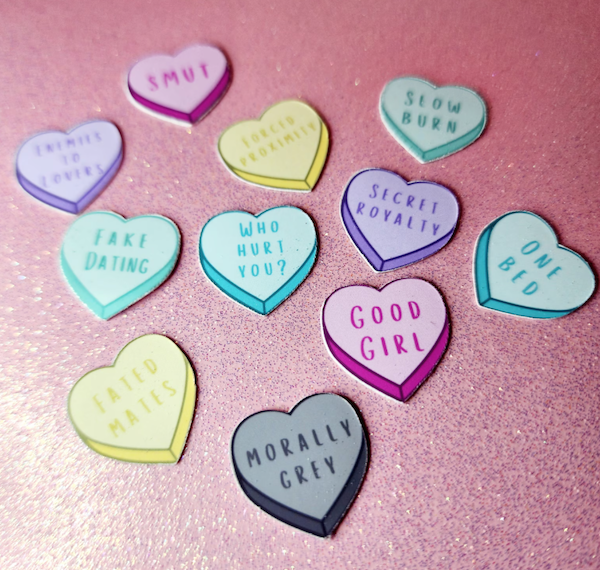 Multicolored conversation heart stickers featuring popular romance trips including "Morally Grey," "One Bed," and "Secret Royalty." 