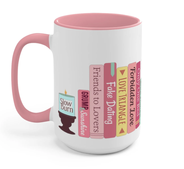 A white mug with pink handle and interior that includes a stack of books that list out popular romance trips including fake dating, friends to lovers, and slow burn. 