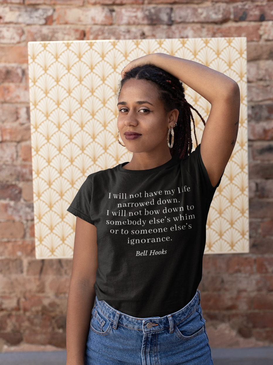 A medium brown-skinned Black woman with her hand over her head, with a t-shirt that has a quote by bell hooks on it