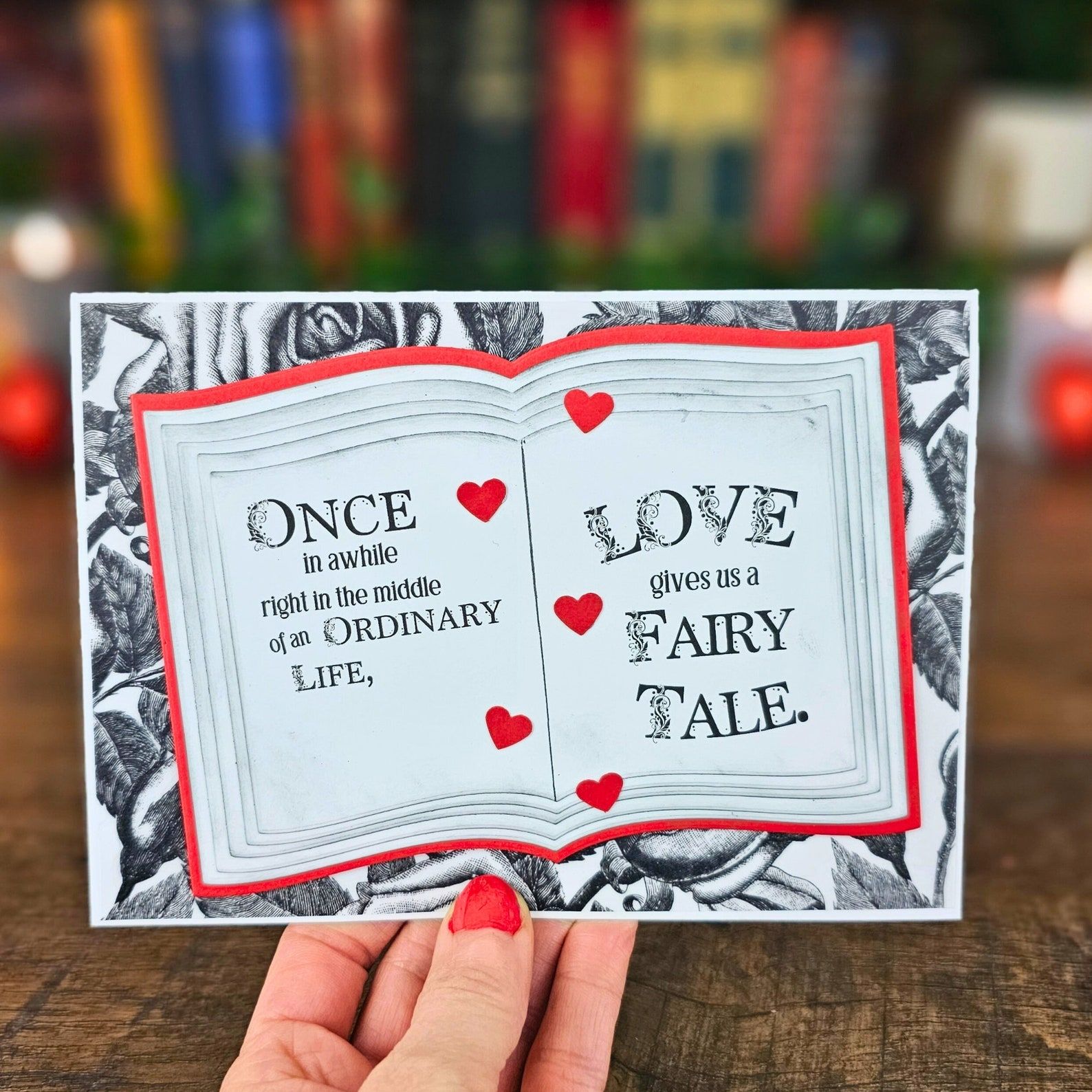 A black, red, and white Valentine of an open book that reads "Once in a while, right in the middle of an ordinary life, love gives us a fairy tale."