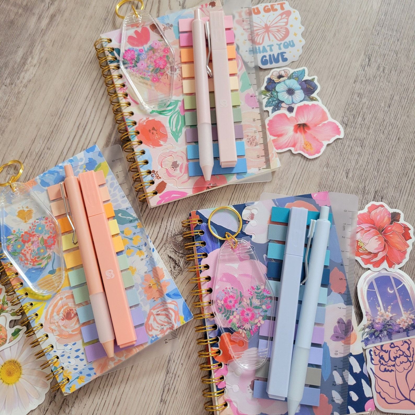 A set of three different floral annotation kits, including pen and highlighter, flags, a notebook, stickers, and a keychain