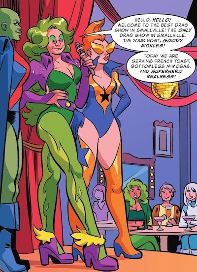 One panel from Fire & Ice #4. There is a stage in the foreground, with Goody Rickels in drag, wearing a low-cut green leotard and tights, purple bolero jacket and heels, a green wig, and lots of green and purple eyeshadow. The outfit is halfway between Fire's costume and Goody's from the cover of Jimmy Olsen #139. She's holding a microphone. There are drag queens dressed as Martin Manhunter and Booster Gold on either side of her. In the background, Fire, Martha, and Ice sit at a small table with cocktails. Fire looks shocked.
Goody: Hello, hello! Welcome to the best drag show in Smallville! The only drag show in Smallville! I'm your host, Goody Rickles! Today we are serving French toast, bottomless mimosas, and superhero realness!