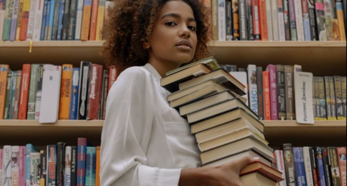 light brown-skinned Black woman holding a stack of books in the library