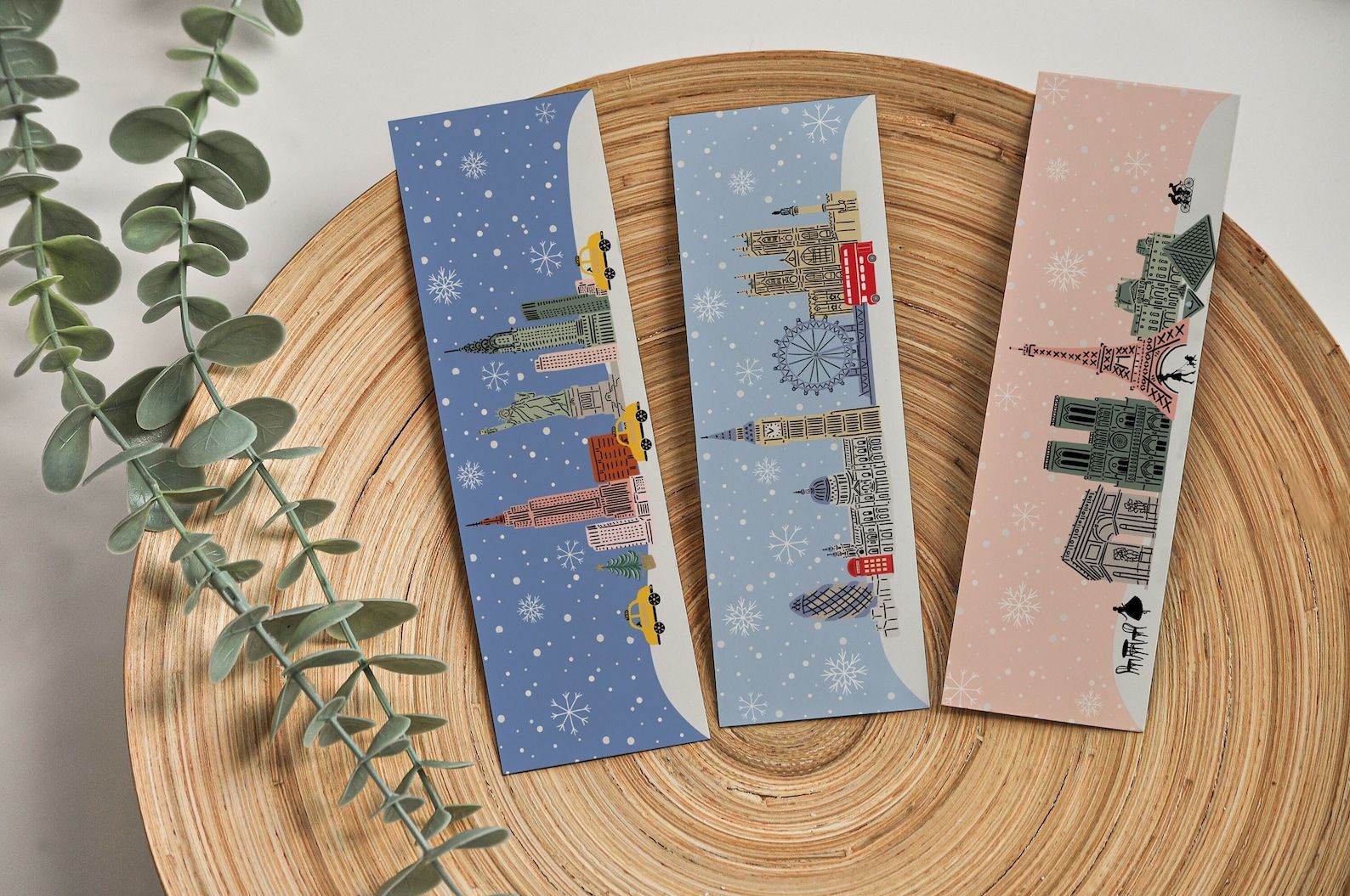 A set of three bookmarks featuring the skylines of NYC, London, and Paris in winter