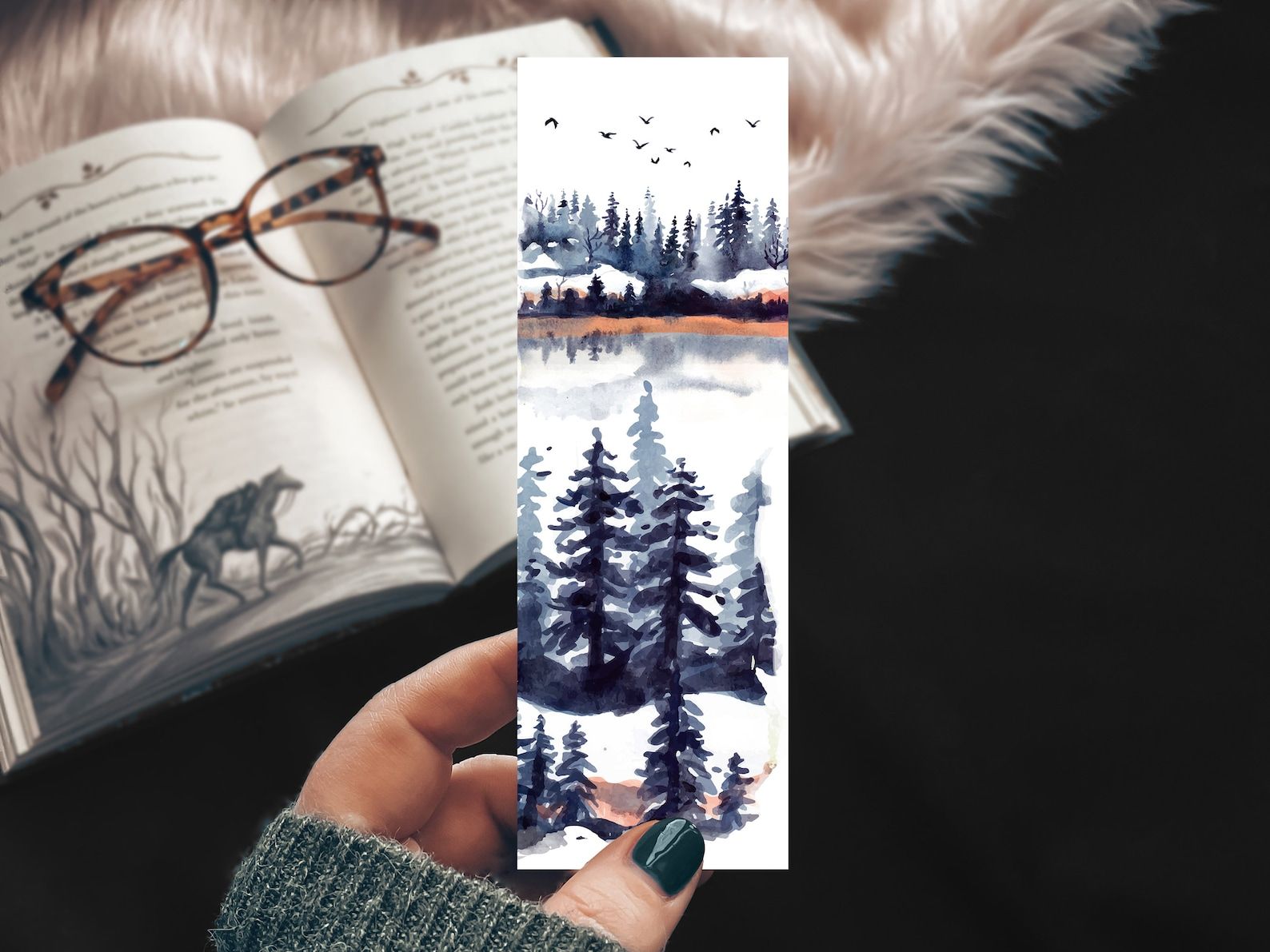 A bookmark with a watercolor landscape of line trees, snow, water, and birds
