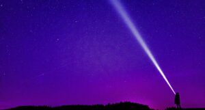 a person shining a bright flashlight into a purple and pink star-filled sky