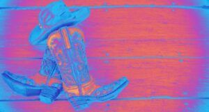 a cowboy hat and cowboy boots against a wood slab background. a nrigh neon blue, pink, and orange filter is applied to the entire image
