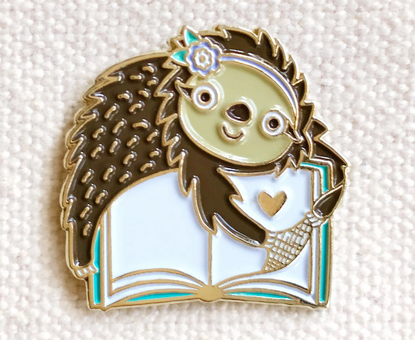 enamel pin of an illustrated sloth turning the page of a book