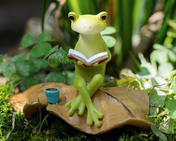 figurine of a frong sitting on a leaf reading a book with a little mug of coffee