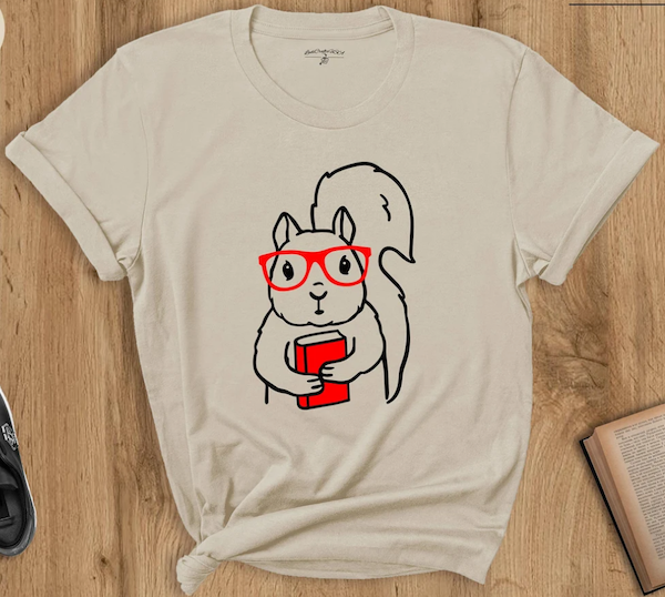 a cream colored tshirt with an illustration of a squirrel in glasses holding a neon orange book