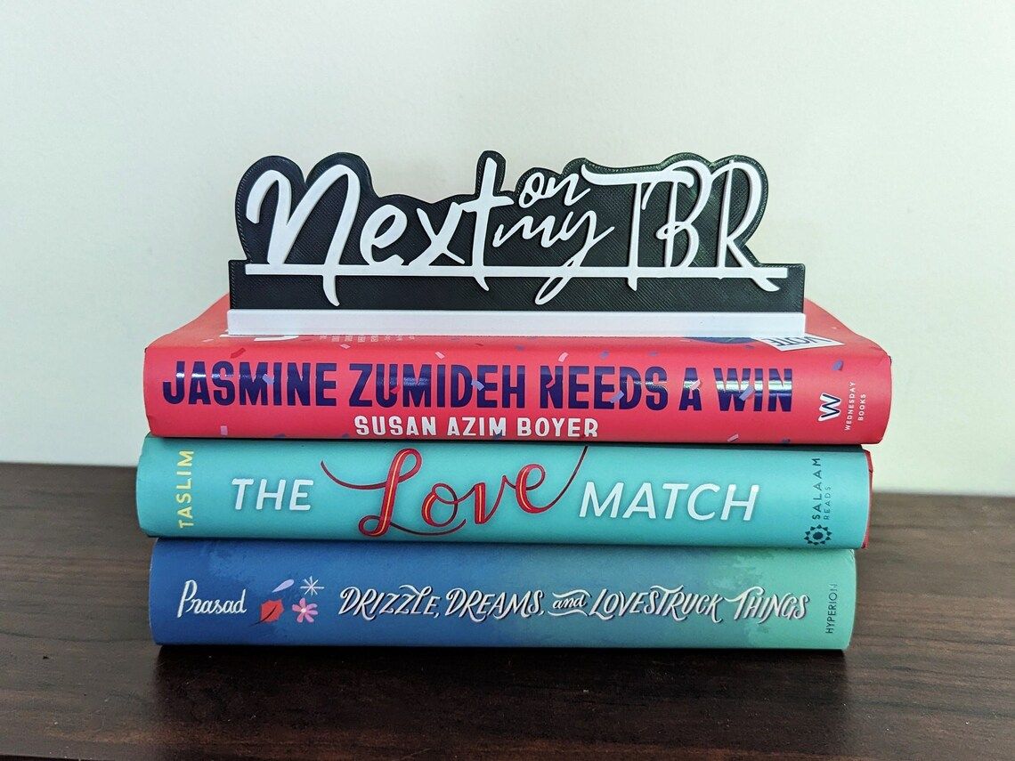 Three books in a stack with a black and white sign on top reading "next on my tbr"