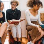 four women of color of various skin tones reading books with each other