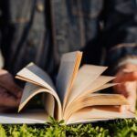 a photo of a book in the grass with an out of focus figure holding it