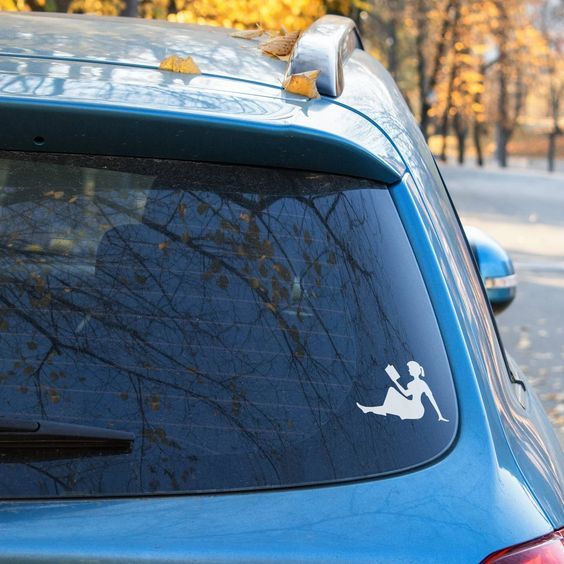 a blue car with a white silhouette of a girl reading a book as a sticker in the corner of the back windshield.