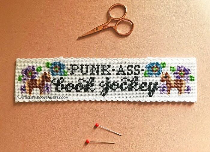 scissors, straight pins, and a cross stitch bookmark that says "punk ass book jockey" and has flowers 