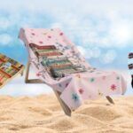 a bookish cornhole set, a chair with a book-print beach towel, and sandals in a bookish print against a blurred beach background